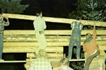 Men placing log during a cabin raising party by Douglas Beck