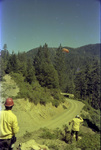 Men watching a smokejumper land in a parachute by Douglas Beck