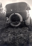One of the official Mitchell Six touring cars sunk in mud on rural dirt road. by Frank W. Guilbert